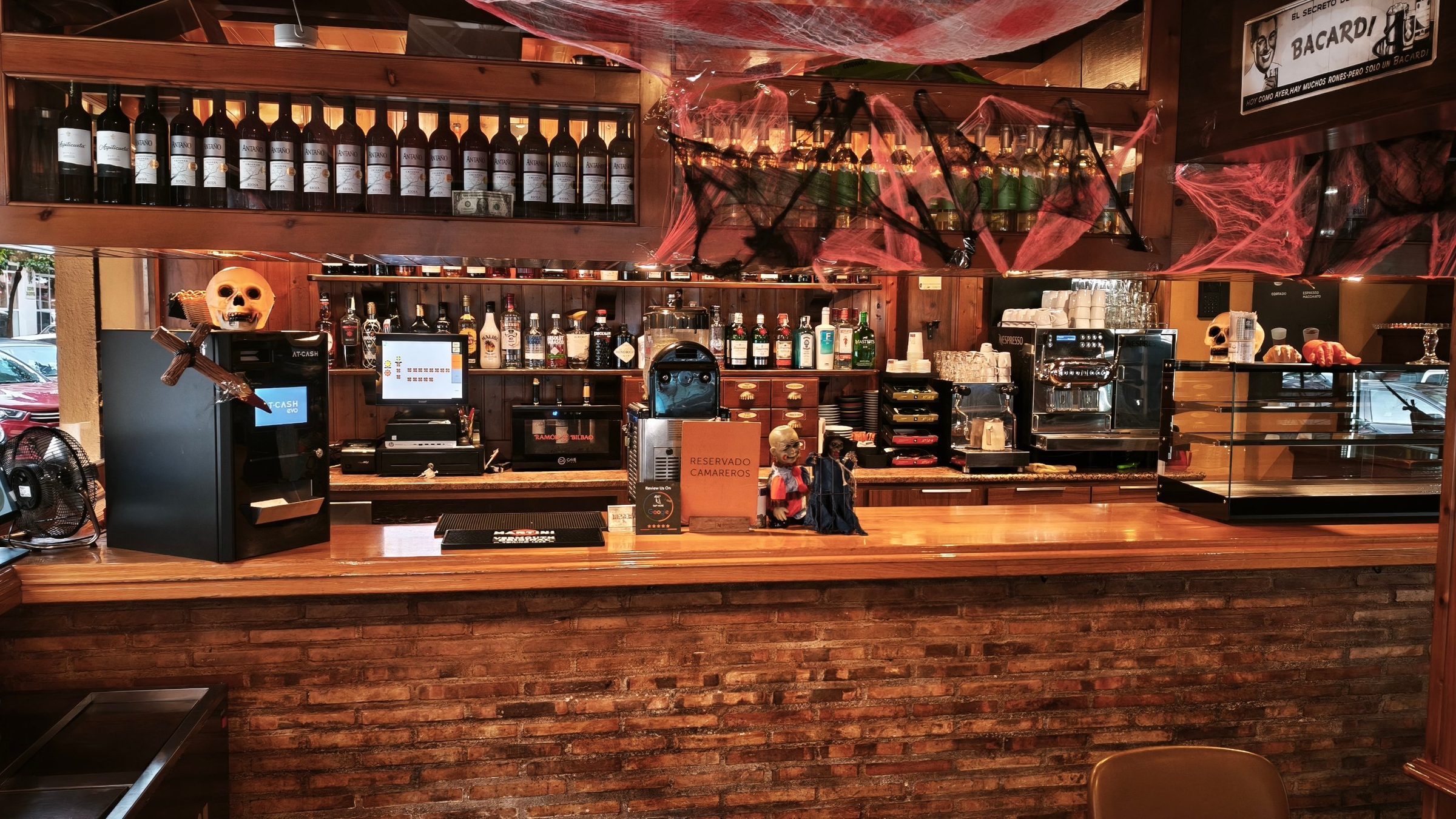 Barra de La Bodeguita de la Esquina con botellas de vino, cafetera y frente de ladrillo