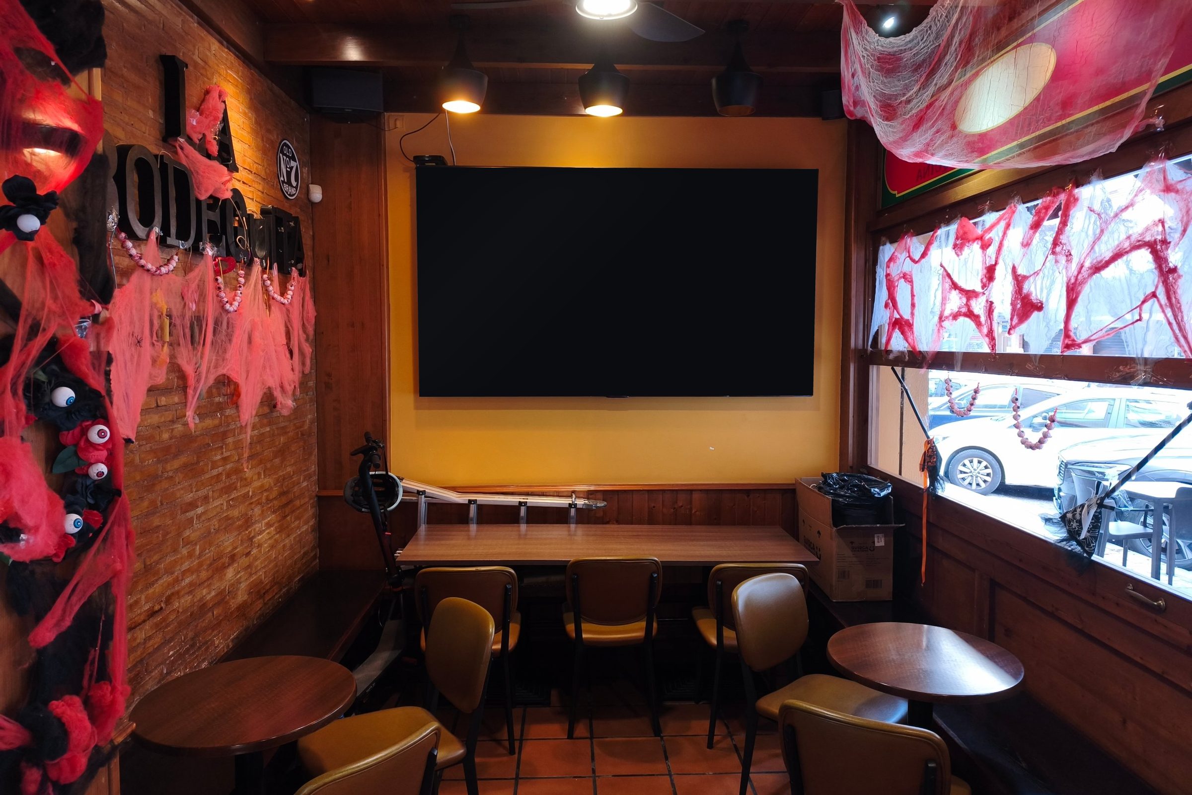 Sala interior con mesas de madera, pared de ladrillo y una tele grande